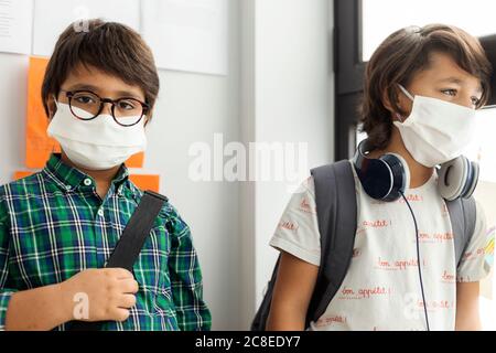 Junge in der Schule mit Freund gegen die Wand stehend Maske Stockfoto