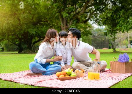 Asiatische Teenager Familie fröhlicher Urlaub Picknick-Moment im Park mit Vater, Mutter küssende Tochter mit Blick auf Kamera und Lächeln, um einen glücklichen Urlaub zu verbringen tim Stockfoto