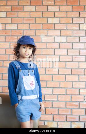 Portrait eines asiatischen Mädchens, das Jeans und eine Mütze trägt, mit Backsteinwand Hintergrund Stockfoto