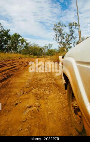 Geländewagen auf rauer Geländebahn im abgelegenen Outback Australiens, mit grüner Buschvegetation, wolkig blauem Himmel als Hintergrund und Kopierraum. Stockfoto