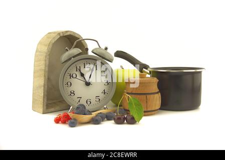 Kulinarisches Stillleben mit altmodischem Wecker, Topf, Apfel, Glas Honig, Kirschen, roten Johannisbeeren und Heidelbeeren auf einem weißen Hintergrund mit Stockfoto