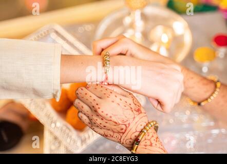 Nahaufnahme der Hände, Schwester, die Rakhi bindet, Raksha bandhan an das Handgelenk des Bruders während des Festivals oder der Zeremonie - Rakshanandhan feierte in ganz Indien als Stockfoto