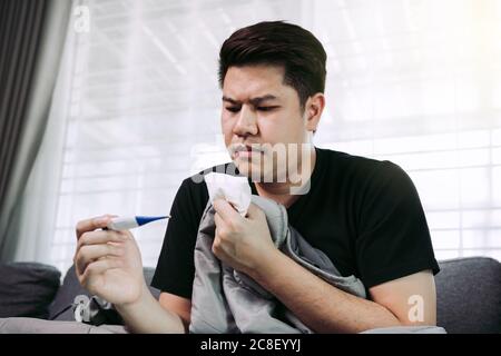 Asiatische Menschen fühlen sich gestresst, weil mit Husten und Erkältung und mit einem Thermometer zu überprüfen, ob er Fieber oder Krankheit in seinem Haus hat. Stockfoto