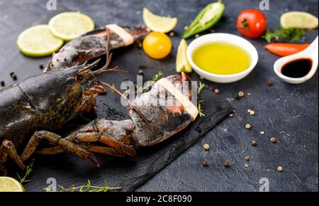 Köstlicher frischer Hummer auf dunklem Hintergrund. Meeresfrüchte mit aromatischen Kräutern, Gewürzen und Gemüse - gesunde Ernährung, Ernährung oder Kochkonzept Stockfoto