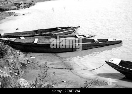 Holzboote in der Nähe eines Flusses. Dieses Bild enthält drei alte Holzboote, die in der Nähe eines Flussufers angedockt sind. Stockfoto