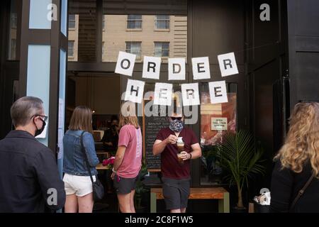 Ein Mann im Gesicht Schal bringt seinen Kaffee auf die Outdoor-Sitzecke im Bijou Cafe in der Innenstadt von Portland, Oregon, am Samstag, 11. Juli 2020. Stockfoto