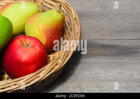 Äpfel und Birnen in einem Korbkorb auf einem rauen Holztisch. Selektiver Fokus. Stockfoto