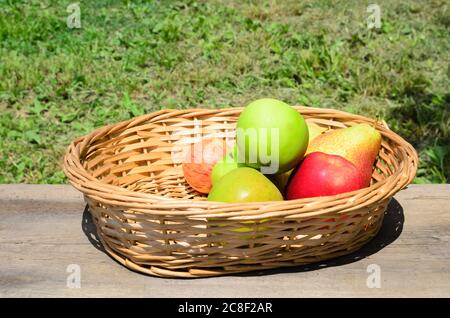 Äpfel und Birnen in einem Korbkorb auf einem rauen Holztisch. Selektiver Fokus. Stockfoto