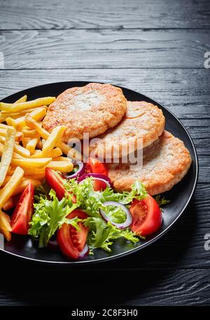 Gebratene Türkei Burger mit Salat Tomate Salat und Pommes frites auf einer schwarzen Platte auf schwarzem Holz Tisch serviert, vertikale Ansicht von oben Stockfoto