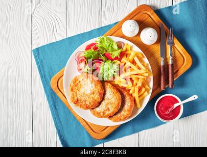 Frisch gebratene drei truthahn Burger mit Salat Tomatensalat und französisch Pommes auf einem weißen Teller auf einem Schneidebrett mit Tomatensauce in Schüssel serviert, ho Stockfoto