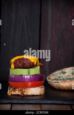 Avocado Burger mit roter Zwiebelscheibe, Burger Bun und Tomate auf einem Holzhintergrund Stockfoto