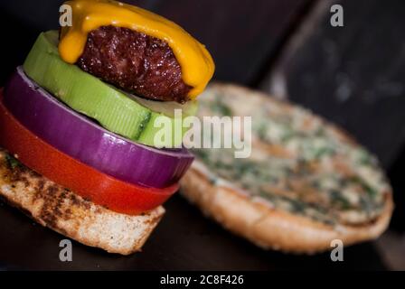 Avocado Burger mit roter Zwiebelscheibe, Burger Bun und Tomate auf einem Holzhintergrund Stockfoto