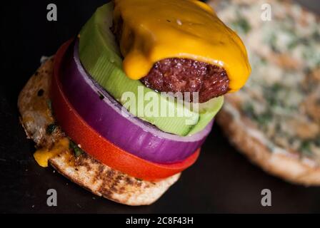 Avocado Burger mit roter Zwiebelscheibe, Burger Bun und Tomate auf einem Holzhintergrund Stockfoto