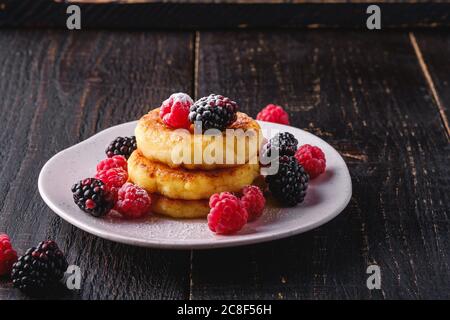 Quark Pfannkuchen und Puderzucker, Quark Fritters Dessert mit Himbeere und Brombeere Beeren in Teller auf dunkelschwarzem Holzhintergrund Stockfoto