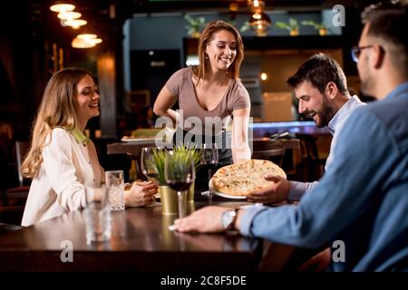 Die nette Kellnerin serviert eine Gruppe von Freunden mit Essen im Restaurant Stockfoto