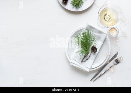 Weihnachtliche Tischeinstellung mit Champagner, Pinienzweigen und Kegeln, Kerzen auf weißem Tisch, Draufsicht, Kopierraum. Weihnachtsessen, Party-Design, Celebra Stockfoto