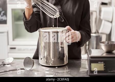 Küchenchefin, die Zutaten in einer Rührschüssel aus Edelstahl mit einem Drahtbesen aus der Nähe in Handschuhen auf ihre Hände bringt Stockfoto