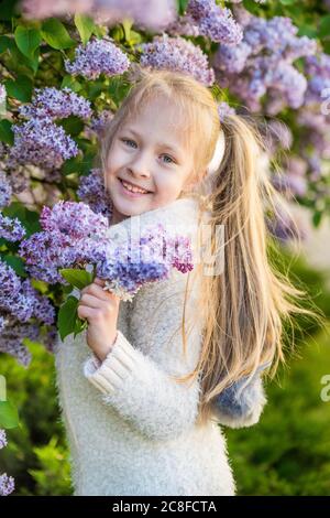 Kleines Mädchen riecht lila Blumen in sonnigen Tag. Stockfoto