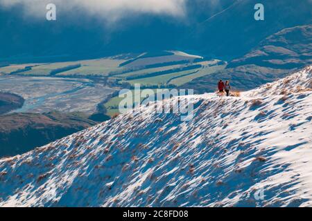 Zwei Touristen laufen auf einem schneebedeckten Weg zum Roys Peak, Wanaka, Neuseeland Stockfoto