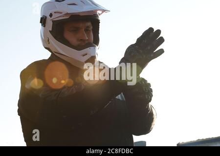 Serious Motorradfahrer im Helm Handschuhe auf die Hände während der Vorbereitung für die Fahrt im Freien, Objektiv Flare-Effekt Stockfoto