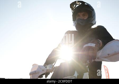 Unten Ansicht der schweren zielgerichteten männlichen Motorradfahrer in Helm und Handschuhe lehnt auf Motorrad in Sonnenlicht Stockfoto