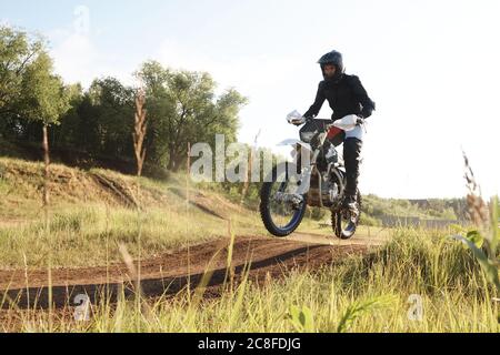 Extreme Mann in Schutzkleidung in der Luft, während Motorrad auf Hügeln bei der Konkurrenz fahren Stockfoto