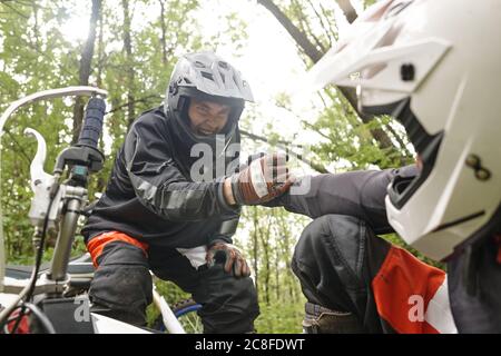 Emotionaler junger Motorradfahrer schreiend, Adrenalin fühlend, während er Freund auf dem Boden Hand gibt Stockfoto