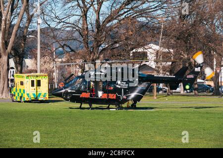 Ein schwarzer MBB BK117 Otago Regional Rescue Helicopter legt einen stationär verbrachten Patienten zu einem wartenden Krankenwagen in Christchurch, Neuseeland ab Stockfoto