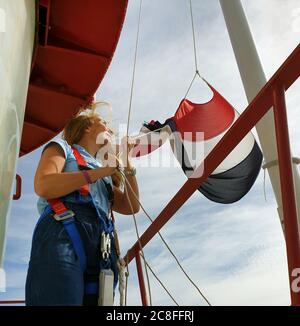 Frau, die die Flagge der Niederlande auf dem Leuchtturm Noordwijk, Niederlande, Noordwijk aan Zee hisst Stockfoto