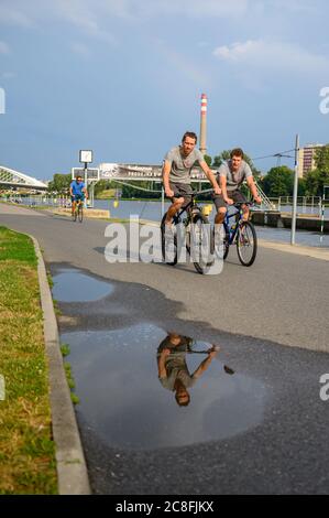 PRAG - 20. JULI 2019: Radfahrer auf einem Flussweg mit Reflexion in Wasserpfütze Stockfoto