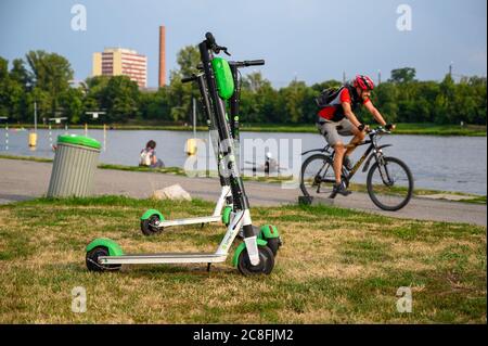 PRAG - 20. JULI 2019: Elektroauto-Roller, die neben einem Mülleimer am Flussufer stehen, mit Radfahrern, die im Hintergrund vorbeifahren Stockfoto