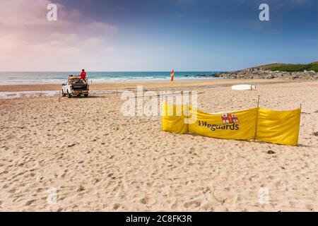 Ein diensthabendes RNLI-Rettungsschwimmer auf der Rückseite eines Rettungswagens am Fistral Beach in Newquay in Cornwall Stockfoto