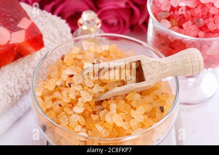 Glasschale mit gelbem Meersalz. Rosa Rosen im Hintergrund. Spa-Zeit Stockfoto