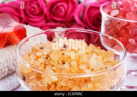 Glasschale mit gelbem Meersalz. Rosa Rosen im Hintergrund. Spa-Zeit Stockfoto