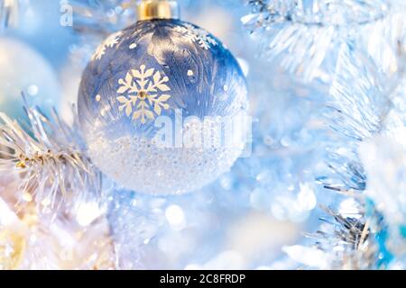 Glänzende Weihnachtskugel in blau, die auf Kiefernästen mit festlichem Hintergrund hängt. Stockfoto