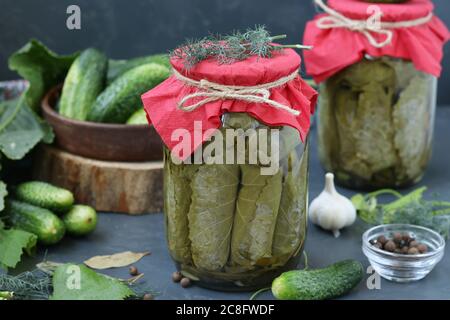 Marinierte Gurken in Traubenblättern mit Knoblauch und Dill in zwei Gläsern auf dunklem Grund, Horizontalformat, Closeup Stockfoto