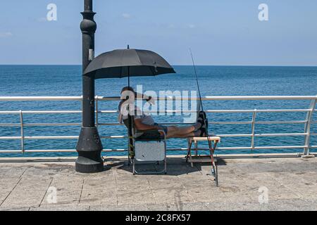 BEIRUT LIBANON. Juli 2020. 24 Ein Fischer untersteht an einem heißen Sommertag unter einem Sonnenschirm mit drückenden Temperaturen über 30Celsius/86Fahrenheit. Kredit: amer ghazzal/Alamy Live Nachrichten Stockfoto