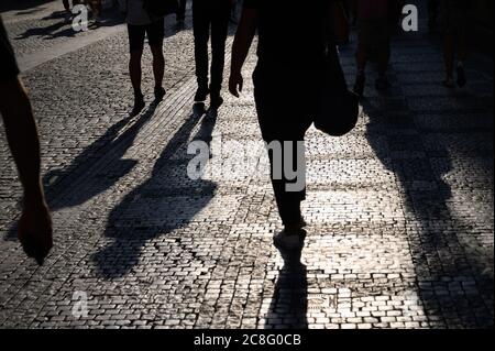 Einfarbige, figurbetonte Beine und lange Schatten über einer alten gepflasterten Straße am frühen Abend bei Sonnenlicht. Stockfoto