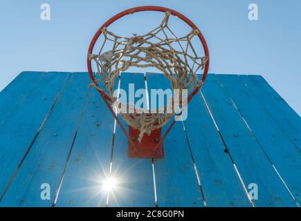 Altes Basketballschild mit einem Ring auf dem Himmel Hintergrund. Sonne scheint durch die Risse zwischen den Brettern. Stockfoto