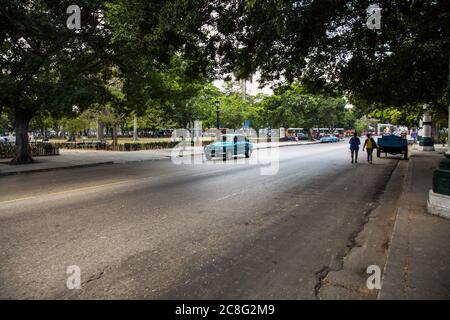 Ein blauer klassischer amerikanischer Wagen, der auf einer alten Asphaltstraße mit Bäumen auf beiden Seiten fährt, Havanna, Kuba Stockfoto