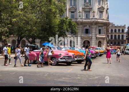 Havanna / Kuba - 04.15.2015: Touristen und Einheimische, die vor bunten klassischen amerikanischen Autos laufen, die als Touristentaxis in Kuba benutzt werden Stockfoto