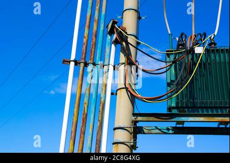 Transformator, Drahtgruppe und Kabel und Pole - Geräte für die elektrische Stromverteilung durch Leitung und Draht. Strahlend blauer Himmel im Hintergrund Stockfoto