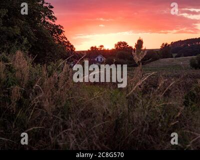 Sonnenuntergang Sonnenaufgang auf einem Getreidefeld auf der Insel Rügen mit einer Farm, Bäumen, Strohballen, roten Mohnblumen nach einem Gewitter Stockfoto
