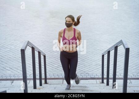 Fit bleiben. Junge Fitness-Frau in Sportkleidung trägt schwarze Schutzmaske läuft oben im Freien während der Coronavirus-Pandemie. Covid 19 und phisical Aktivität, Sport, gesunde Lebensweise Stockfoto