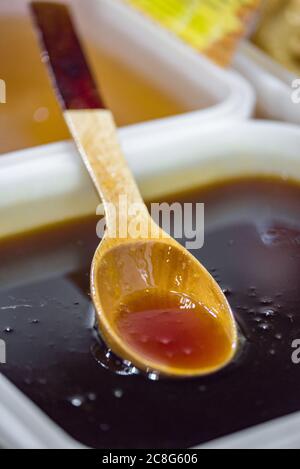 Glänzendes goldenes Honig tropft von einem Holzlöffel in eine Plastikschale. Stockfoto