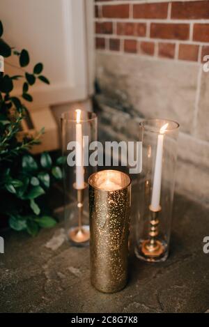 Nahaufnahme von Hochzeitsdekorationen, weißen Kerzen im Glas und goldenen Kerzenhaltern. Stockfoto