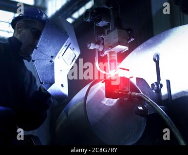 Mann mit Schweißmaske, der in einer Stahlfabrik arbeitet. Stockfoto