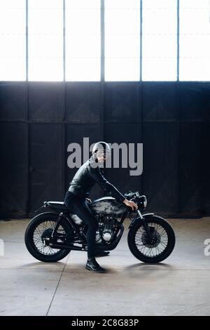 Junge männliche Motorradfahrer auf vintage Motorrad in leere Lager, Porträt Stockfoto