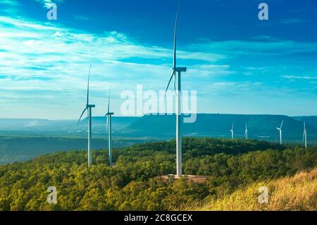 Landschaft der Windmühle mit grünem Wald und klaren blauen Himmel über dem Berg. Elektrische Windkraftanlagen über dem Damm. Stockfoto