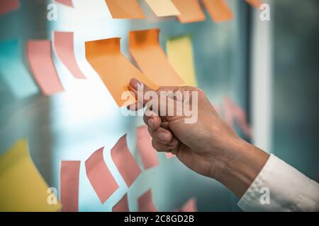 Weibliche Hand klebt leere Aufkleber auf dem Bürofenster. Viele bunte Notizpapier-Aufkleber mit Platz für Text auf Glaswand geklebt. Getöntes Bild Stockfoto